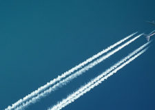 A plane cuts diagonally across a deep blue sky, leaving contrails behind it