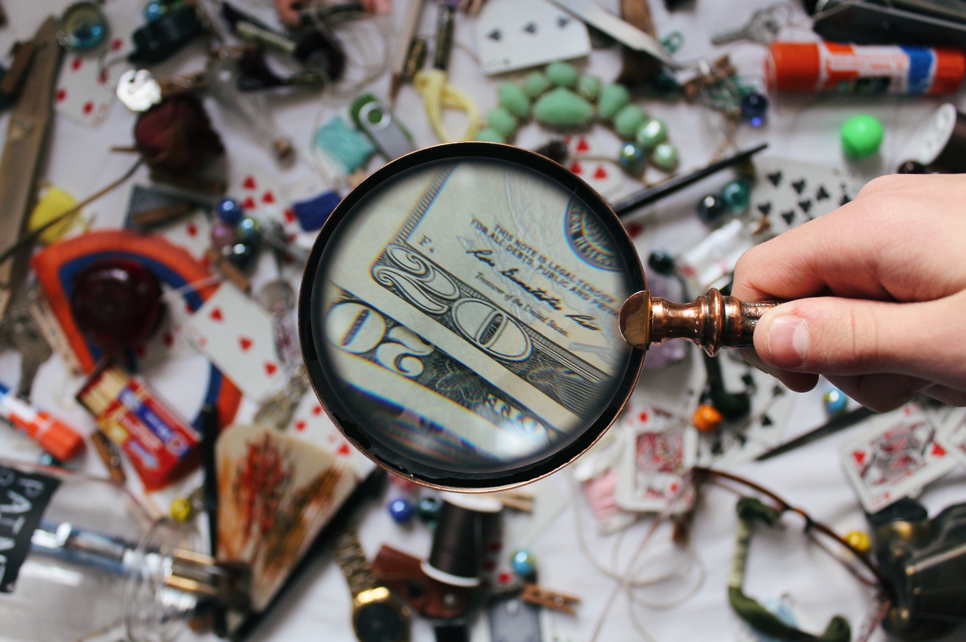 Magnifying glass spotting dollar bills amid a mess of objects