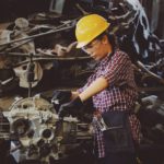 woman engineer working on engine in factory wearing a heard helmet