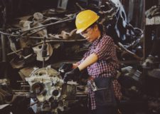 woman engineer working on engine in factory wearing a heard helmet