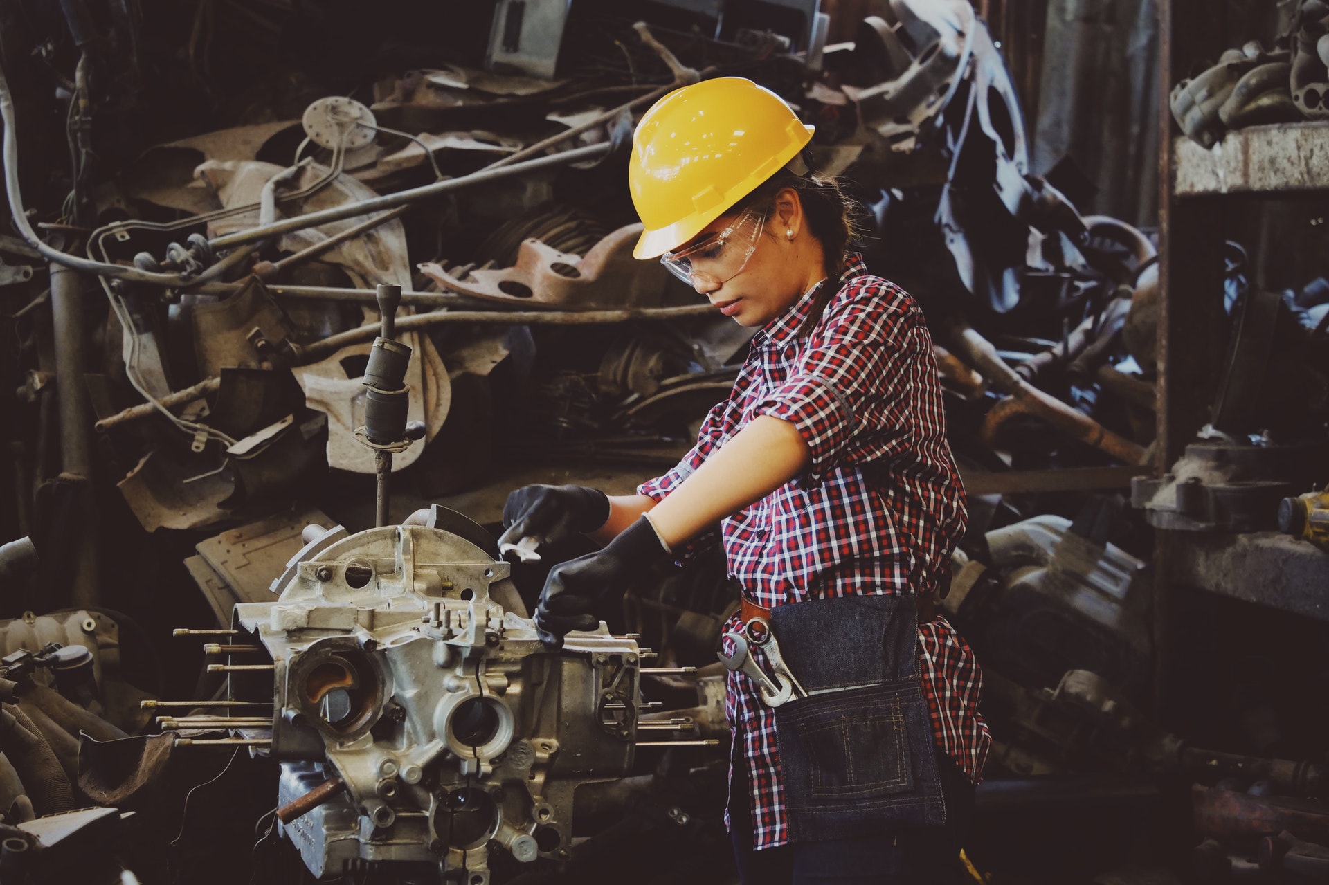 woman engineer working on engine in factory wearing a heard helmet