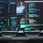 Glasses frame on a desk in front of a busy computer screen displaying code