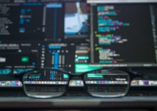 Glasses frame on a desk in front of a busy computer screen displaying code
