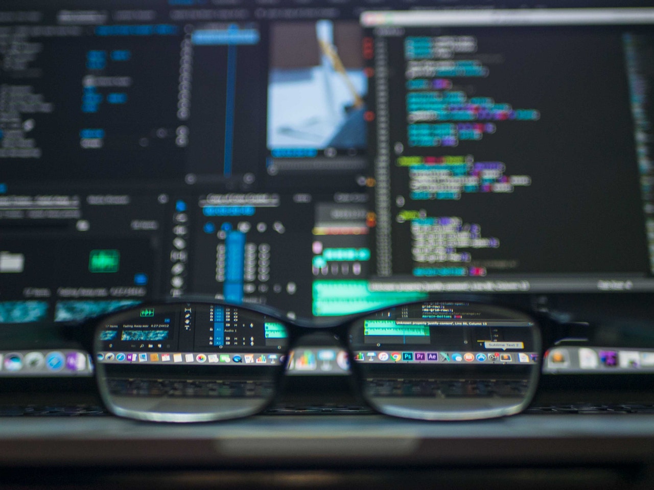 Glasses frame on a desk in front of a busy computer screen displaying code