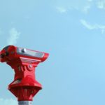 A red coin operated binocular against a bright blue sky