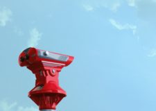 A red coin operated binocular against a bright blue sky