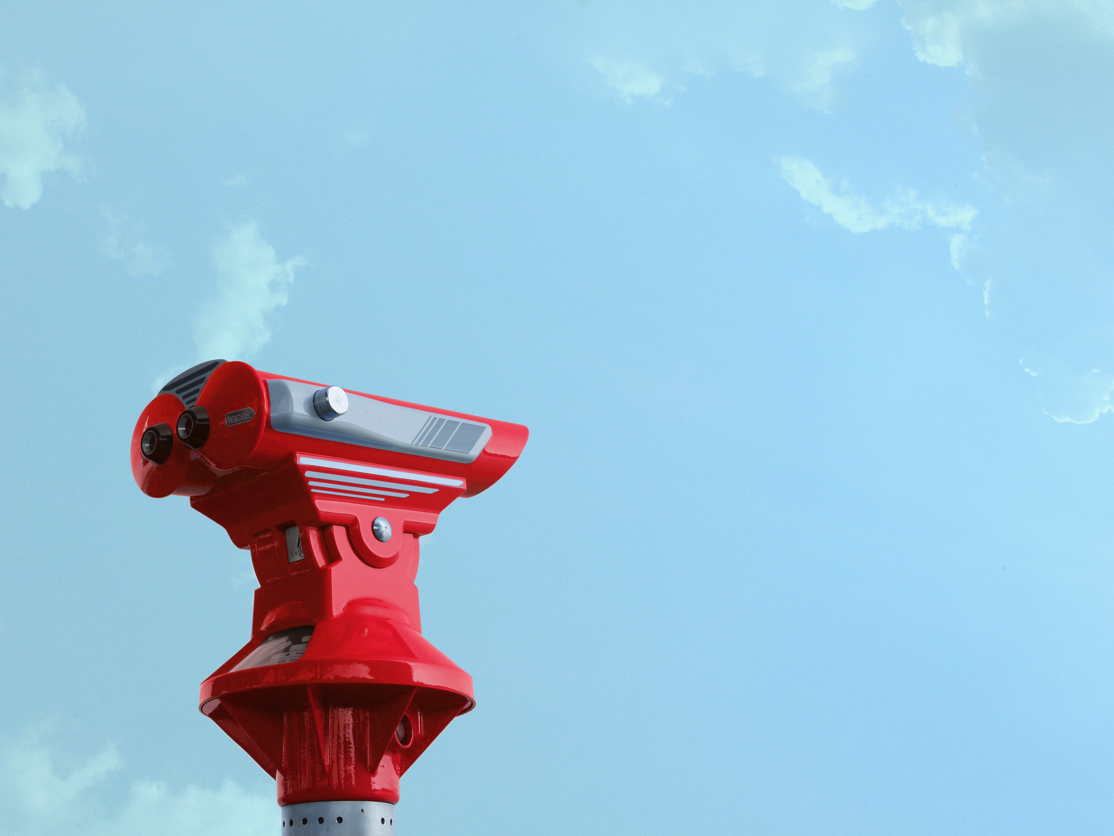 A red coin operated binocular against a bright blue sky