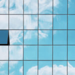 A single open window in a grid of closed glass windows mirroring the sky