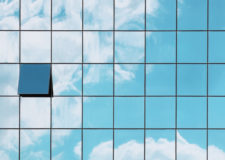 A single open window in a grid of closed glass windows mirroring the sky